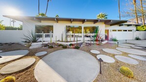 Ein modernes Haus mit flachem Dach, großen Fenstern und einem Garten mit Kakteen und Palmen.