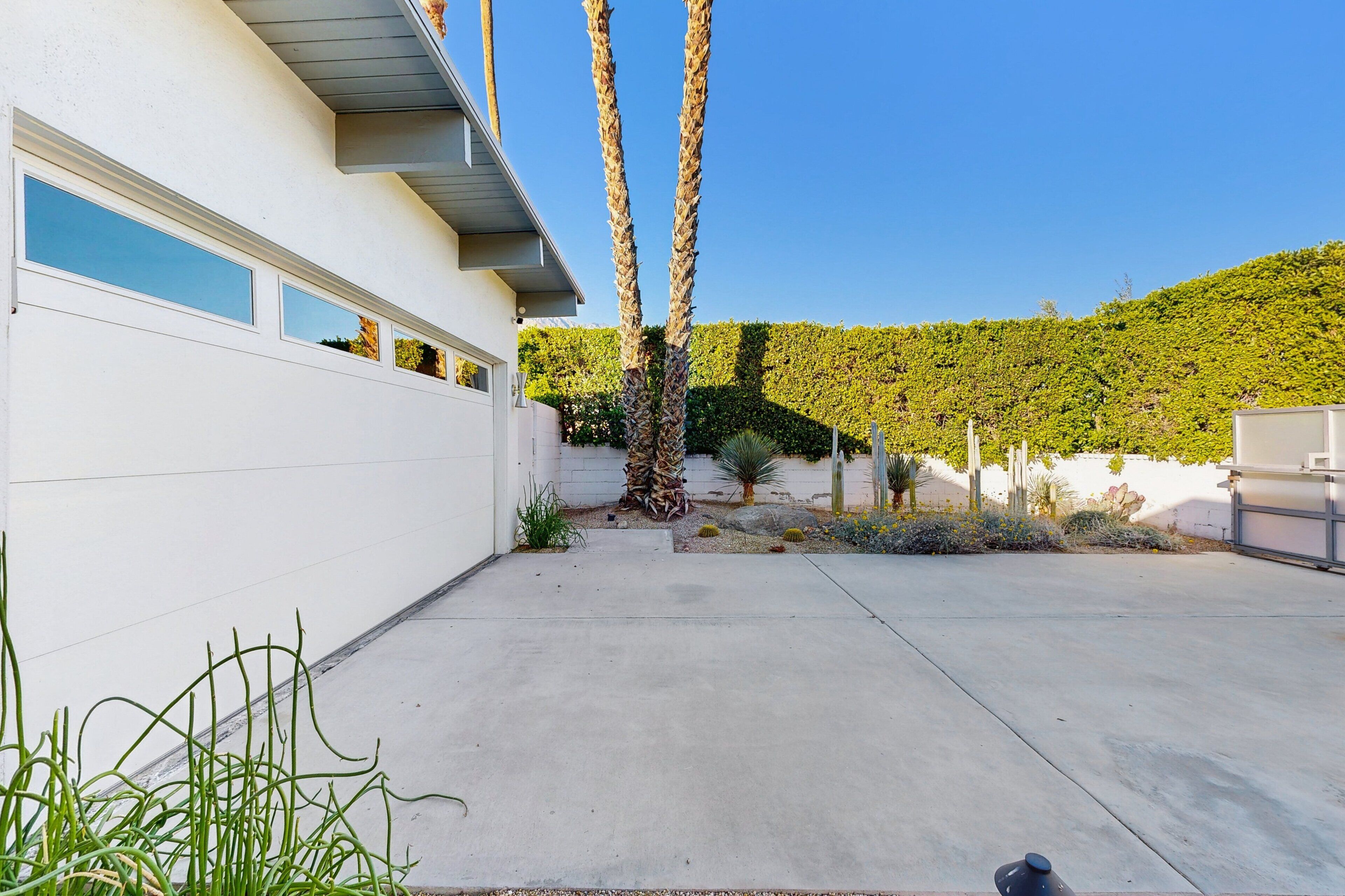 Ein modernes Haus mit weißer Fassade, einer Garage und einem gepflegten Garten mit Palmen und Sträuchern.