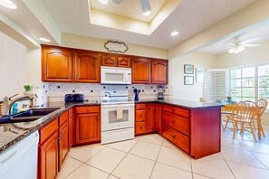 A kitchen with wooden cabinets, a microwave, a stove, and a dining area with chairs and a table. - Ground-floor mountain view condo with a pool, hot tub, tennis, & fitness room (Palm Desert)