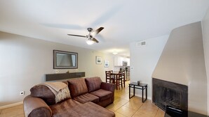 A living room with a brown leather sofa, a ceiling fan, a fireplace, and a dining area with chairs and a table. - Sun Valley condo with a patio, washer/dryer, & AC - pool, hot tub, grill access (Scottsdale)