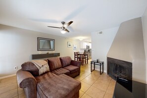 A living room with a brown leather sofa, a ceiling fan, a fireplace, and a dining area with chairs and a table. - Sun Valley condo with a patio, washer/dryer, & AC - pool, hot tub, grill access (Scottsdale)