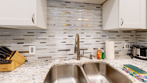 A kitchen with white cabinets, a stainless steel sink, a modern faucet, and a tiled backsplash. - Sun Valley condo with a patio, washer/dryer, & AC - pool, hot tub, grill access (Scottsdale)