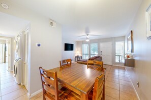 A dining area with a wooden table and chairs, a ceiling fan, and a television mounted on the wall. - Sun Valley condo with a patio, washer/dryer, & AC - pool, hot tub, grill access (Scottsdale)