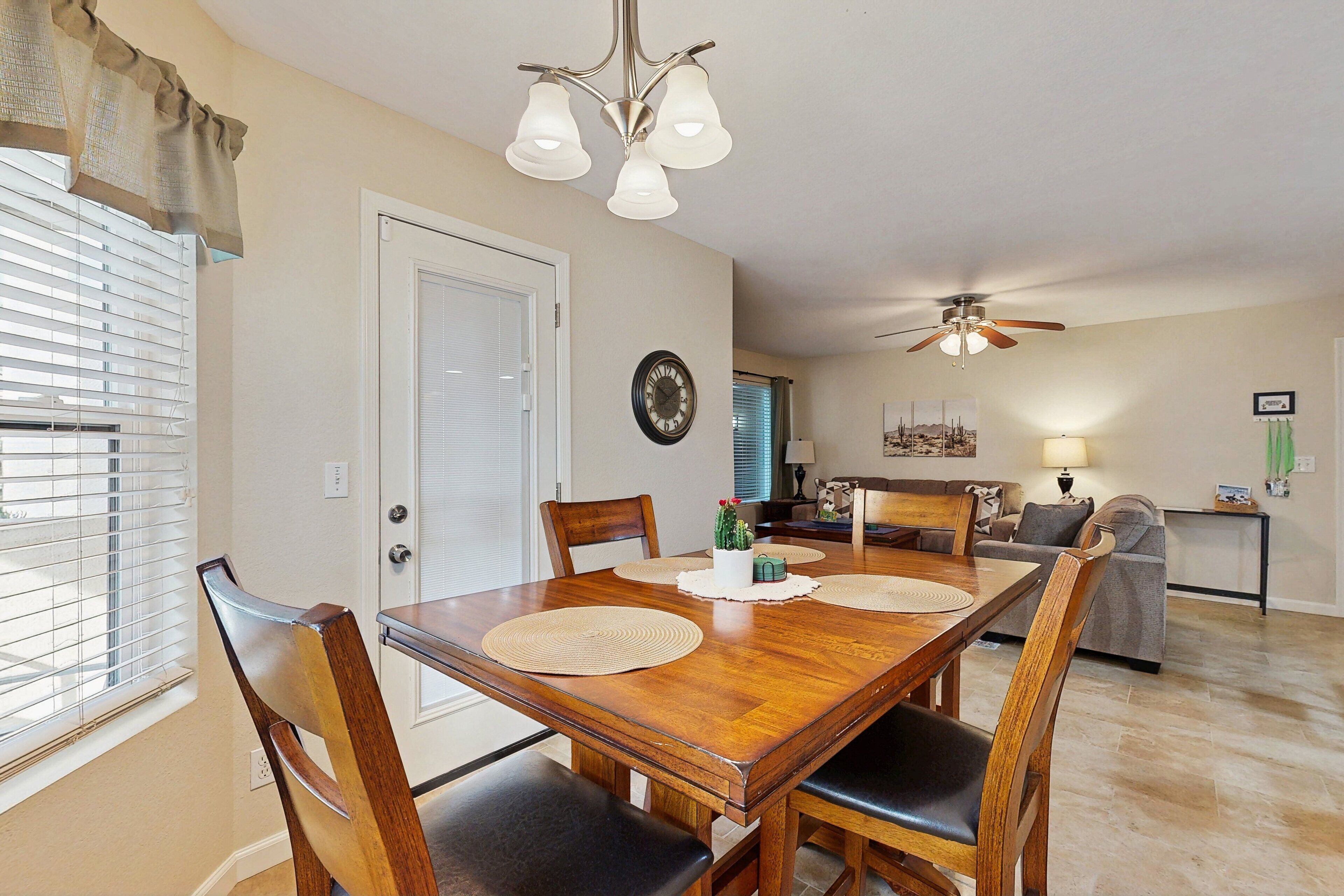 A dining area with a wooden table, chairs, a chandelier, and a ceiling fan.