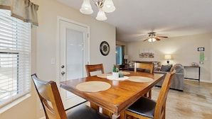 Un espace repas comprenant une table en bois, des chaises, un lustre et un ventilateur de plafond.