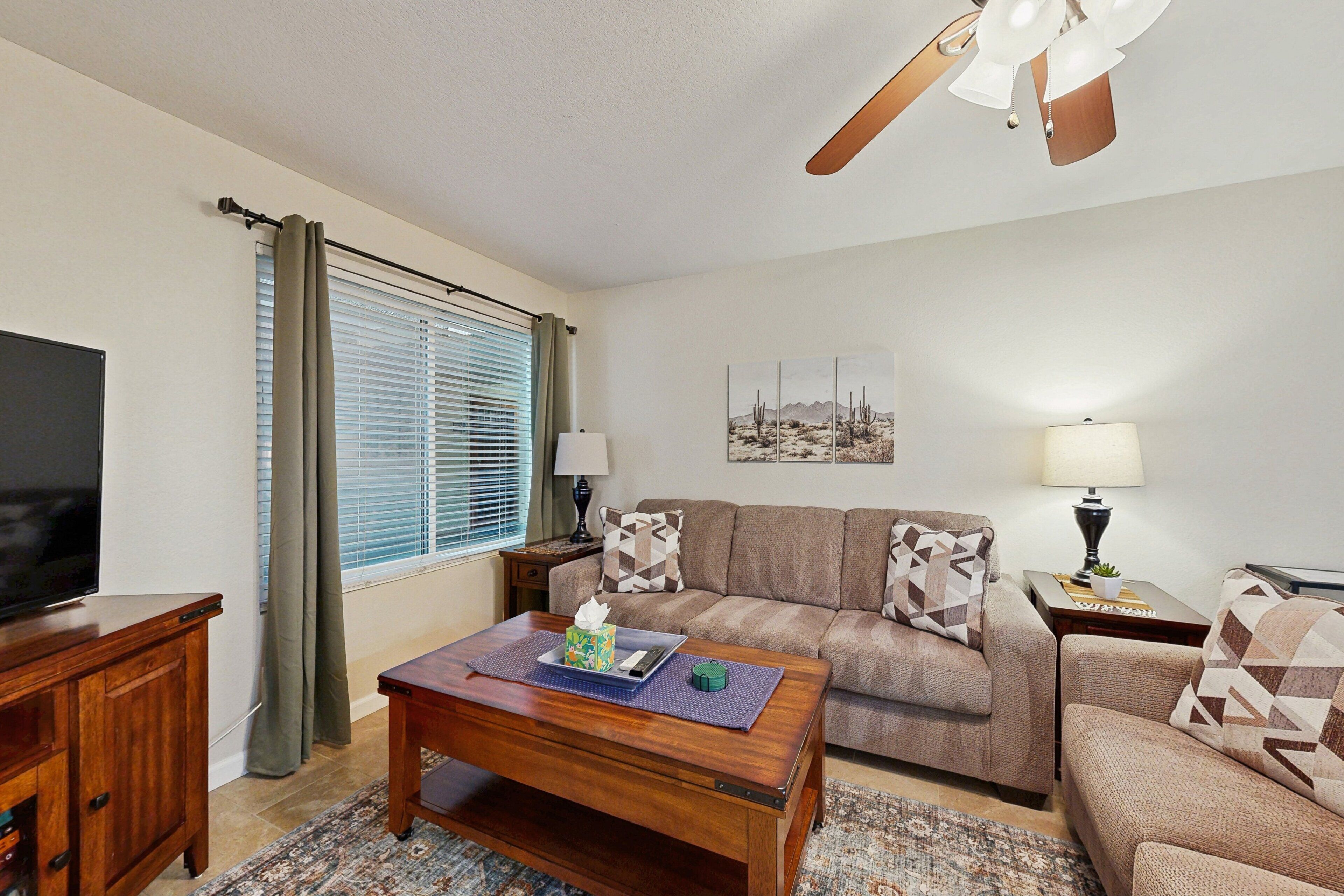 A living room with a television, a sofa, a coffee table, and a ceiling fan.