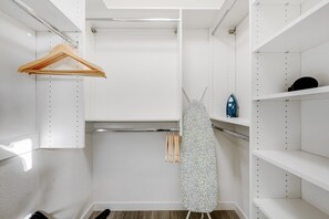 A walk-in closet with white shelving, a wooden hanger, and a patterned garment hanging on a rod. - Lovely, updated home with enclosed yard, fast WiFi, W/D, & mountain view (Scottsdale)