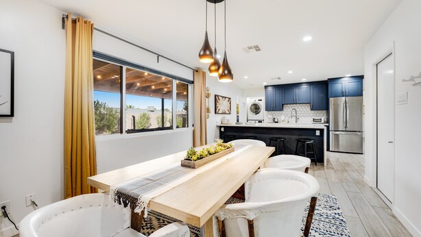A modern kitchen with a long wooden table, white chairs, and a central island. - Lovely, updated home with enclosed yard, fast WiFi, W/D, & mountain view (Scottsdale)