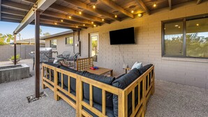An outdoor patio with a wooden bench, a table, and a flat-screen TV mounted on the wall. - Lovely, updated home with enclosed yard, fast WiFi, W/D, & mountain view (Scottsdale)