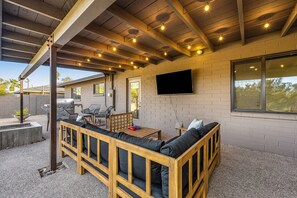 An outdoor patio with a wooden bench, a table, and a flat-screen TV mounted on the wall. - Lovely, updated home with enclosed yard, fast WiFi, W/D, & mountain view (Scottsdale)