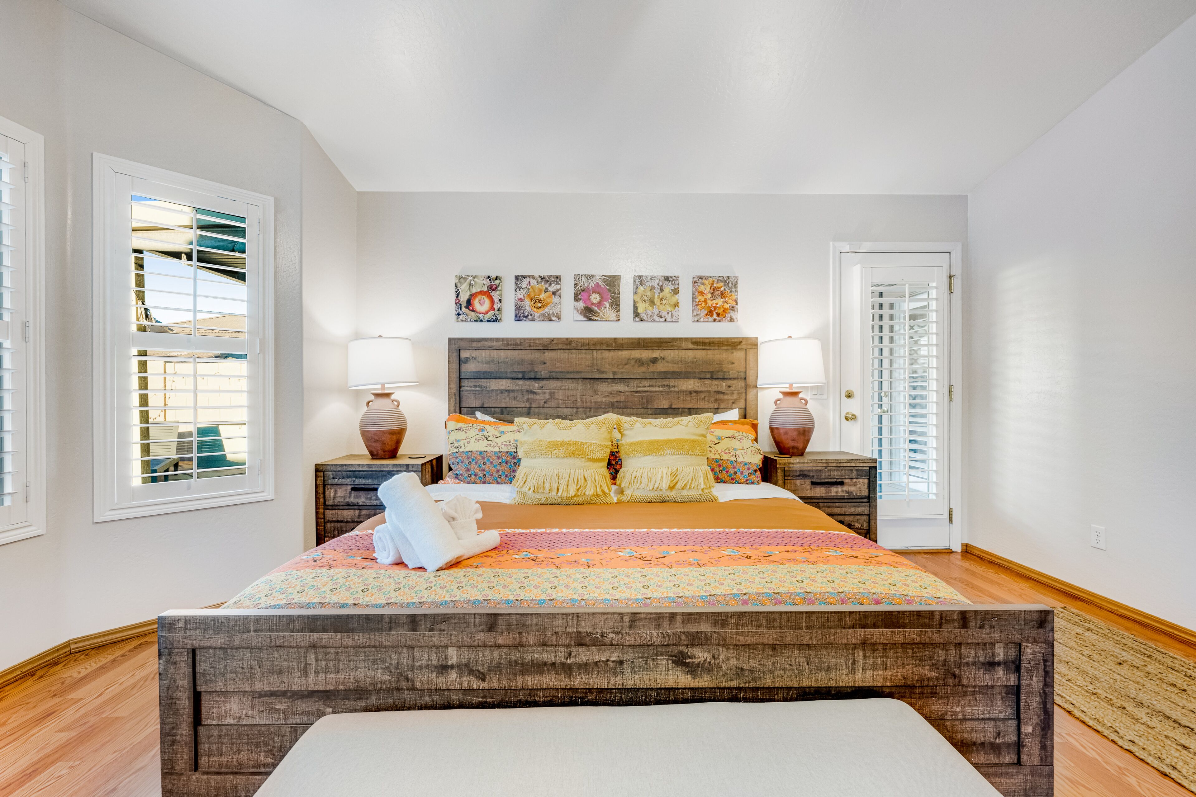 A bedroom with a wooden headboard, a floral bedspread, and a set of four wall-mounted paintings.