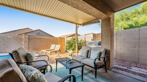 Uma área de pátio externa com espaço de estar coberto, piscina e vista para as casas vizinhas.