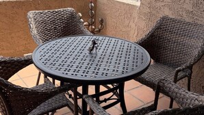 Una mesa y sillas de mimbre en un balcón, con una piscina al fondo.