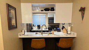 Una cocina compacta con una isla central, dos taburetes de bar, un fregadero y un ventanal.
