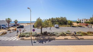 Una carretera costanera amb un ciclista, cotxes aparcats i un pas de vianants.