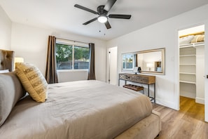 A bedroom with a large bed, a ceiling fan, a bedside table with a lamp, a mirror, and a walk-in closet. - Stylish desert oasis with fast WiFi, fenced yard, & screened patio (Scottsdale)