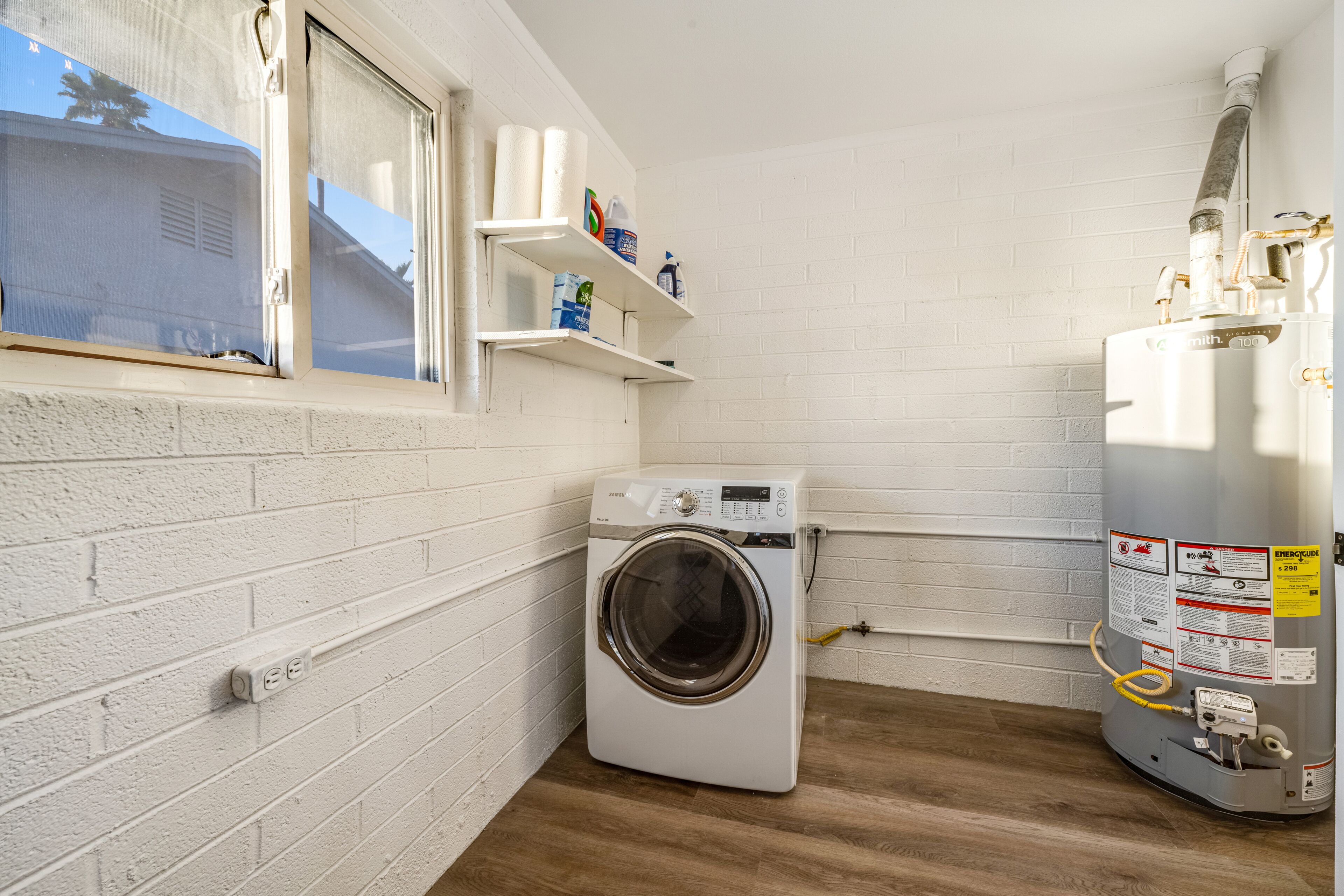 A compact laundry room with a washing machine, a water heater, and a window with a view.