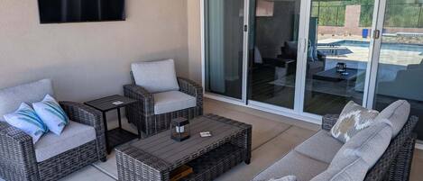 Un espace patio aménagé avec des meubles en osier, une table basse et une porte-fenêtre coulissante donnant accès à une piscine.