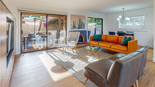 Uma sala de estar moderna com um sofá, mesa de centro e cadeiras. Há uma porta de vidro deslizante que dá para uma área externa com uma mesa e cadeiras.