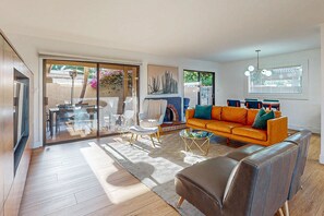 Una sala de estar moderna con sofá, mesa de centro y sillas. Posee un ventanal corredero que da a un espacio exterior con mesa y sillas.
