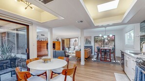 Uma sala de estar ampla com uma mesa de jantar, cadeiras de madeira, cozinha e uma janela grande.