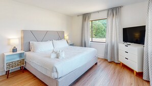 Quarto moderno com cama grande, mesas de cabeceira, televisão e janela com cortinas.