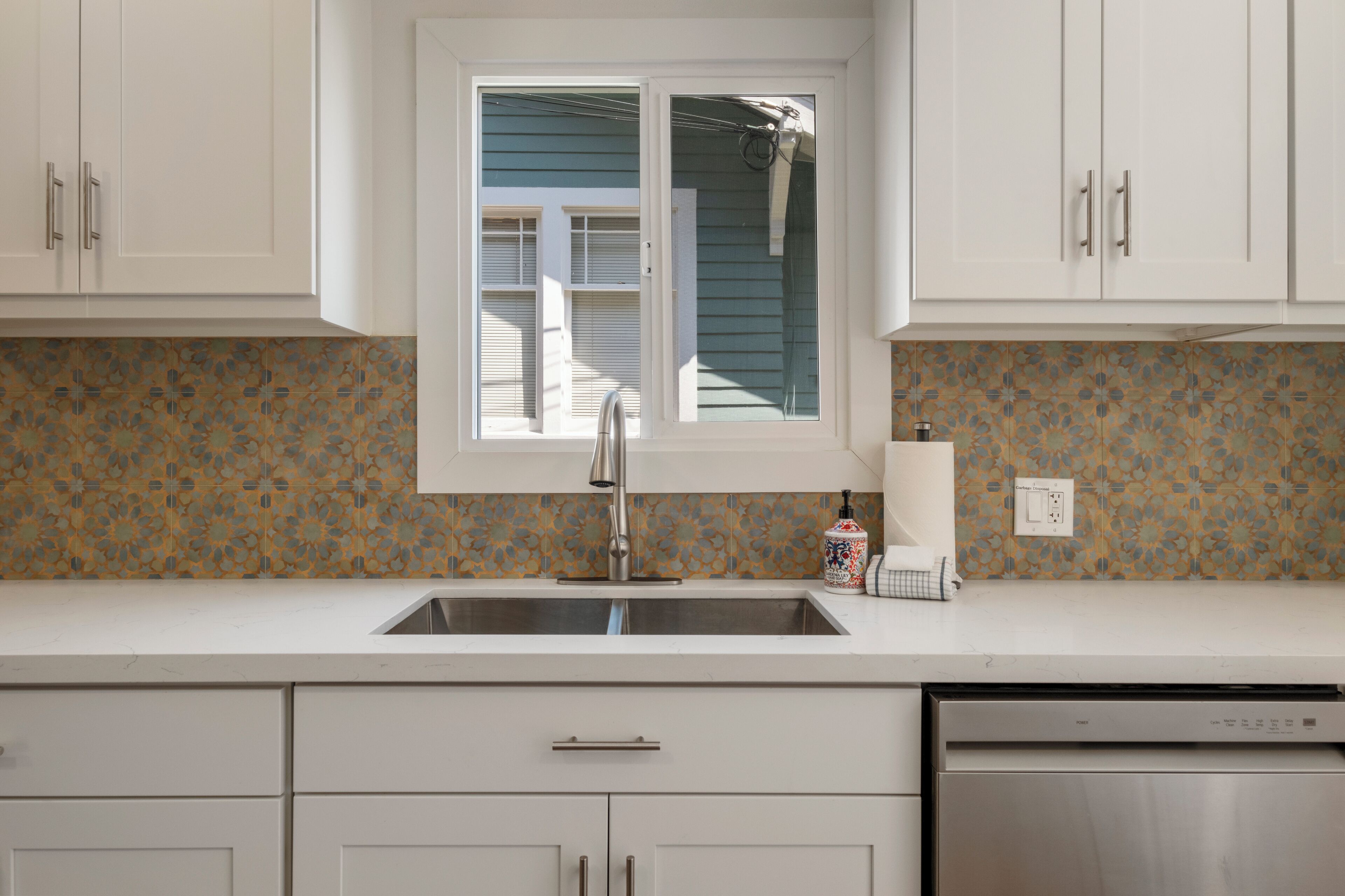 A kitchen with white cabinets, a stainless steel sink, and a window above the countertop.