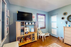 A room with a television on a stand, a bookshelf, a white chair, and a door with a window. - Charming home with large yards and excellent location for any interests (Phoenix)