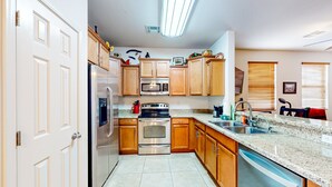 A modern kitchen with wooden cabinets, stainless steel appliances, a granite countertop, and a built-in dishwasher. - Desert retreat with enclosed yard, instruments, alfresco dining, grill, & W/D (San Tan Valley)