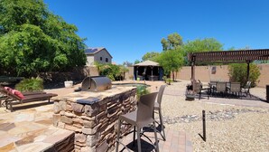 Eine Terrassenanlage mit Steinsitzgelegenheiten, einem Grill und einer Pergola.