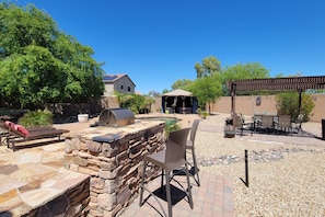 A patio area with stone seating, a grill, and a pergola. - Spectacular oasis with private pool, large yard, & game room (Surprise)