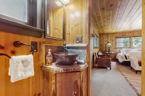 A wooden cabin interior with a rustic bathroom, a wooden dining table, and a cozy living area with a sofa and a lamp. - Fantastic wooded escape with private hot tub, WiFi & deck (Idyllwild)