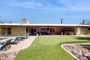 Ein Gebäude mit einer Terrassenanlage, auf der Liegestühle und ein Putting-Green zu finden sind.