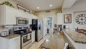 A modern kitchen with white cabinets, stainless steel appliances, granite countertops, and a clock on the wall. - Dog-friendly, ground-floor condo with patio, desert views, pool, hot tub, & W/D (Oro Valley)