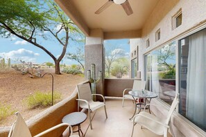Une terrasse couverte avec des chaises et une table, un ventilateur de plafond et une vue sur un paysage désertique.