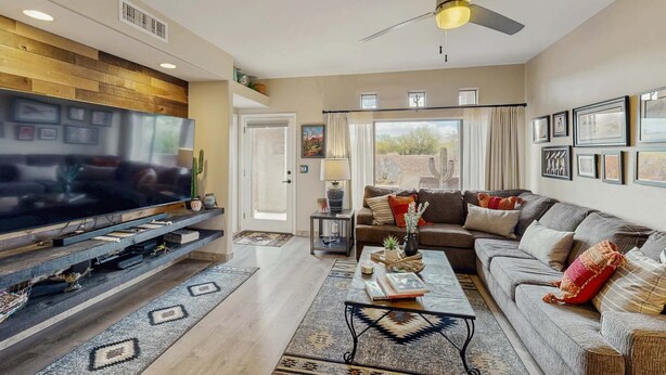 A living room with a flat-screen TV, a ceiling fan, a sofa, and a coffee table. - Dog-friendly, ground-floor condo with patio, desert views, pool, hot tub, & W/D (Oro Valley)