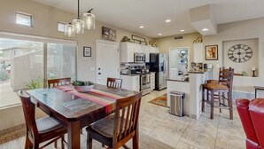 A modern kitchen with white cabinets, a dining area with a wooden table and chairs, and a large window providing a view of the outside. - Dog-friendly, ground-floor condo with patio, desert views, pool, hot tub, & W/D (Oro Valley)