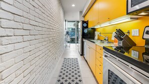 Una cocina estrecha, con una pared de ladrillo en un lado y armarios amarillos en el otro.