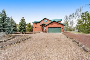 A two-story house with a green garage door, surrounded by a gravel driveway and trees.