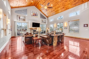 A spacious living room with a wooden ceiling, large windows, and a fireplace.