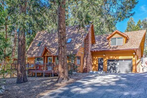 A log cabin with a garage, surrounded by tall trees.
