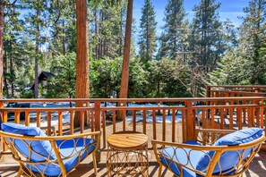 A wooden deck with wicker chairs and a small table, surrounded by tall trees.