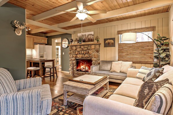 A cozy living room with a stone fireplace, wooden ceiling beams, and a comfortable seating area.
