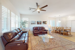 A spacious living room with a brown leather sofa, a glass coffee table, and a dining area with wooden chairs and a table. - Vistoso Preserve Casita #220C | Condo in Oro Valley (Oro Valley)