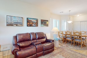 A living room with a brown leather sofa, a dining table with wooden chairs, and three framed artworks on the wall. - Vistoso Preserve Casita #220C | Condo in Oro Valley (Oro Valley)