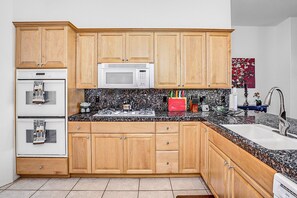 A kitchen with wooden cabinets, a microwave, a stove, a sink, and a granite countertop. - Peaceful, dog-friendly home with private pool, attached spa & patio (Palm Desert)