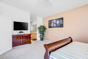 A bedroom with a bed, a dresser, a television, a potted plant, and a wall-mounted painting. - Peaceful, dog-friendly home with private pool, attached spa & patio (Palm Desert)
