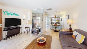Un salon moderne avec un téléviseur  à écran plat, un canapé, une table basse et un coin repas à l’arrière-plan.