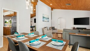 Un comedor moderno con una mesa de madera preparada para seis personas, un sofá gris y un televisor de pantalla plana montado en la pared.