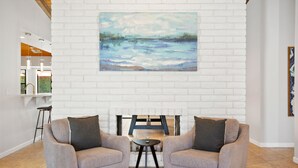 Un vestíbulo con dos sillones orientados hacia una pared de ladrillo blanco, un cuadro sobre los sillones y una pequeña mesa entre ellos.